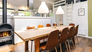 A modern kitchen with a wood-burning stove, a dining table with chairs, pendant lights, and a view of the outdoors. - 10 Person Holiday Home in Fjerritslev (Fjerritslev)