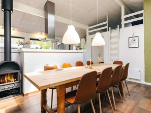 Una cocina moderna con estufa de leña, una mesa de comedor con sillas, lámparas colgantes y vistas al exterior.