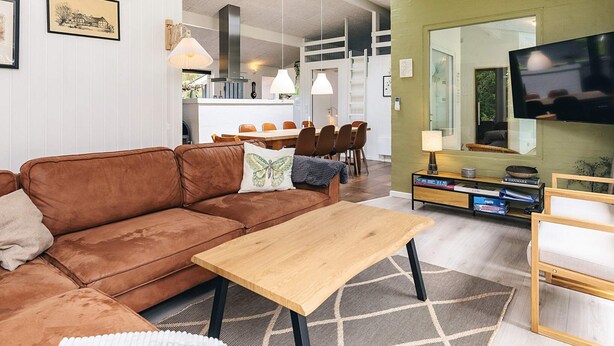 A modern living room with a brown sofa, a wooden coffee table, a TV, and a dining area with chairs and a table. - 10 Person Holiday Home in Fjerritslev (Fjerritslev)