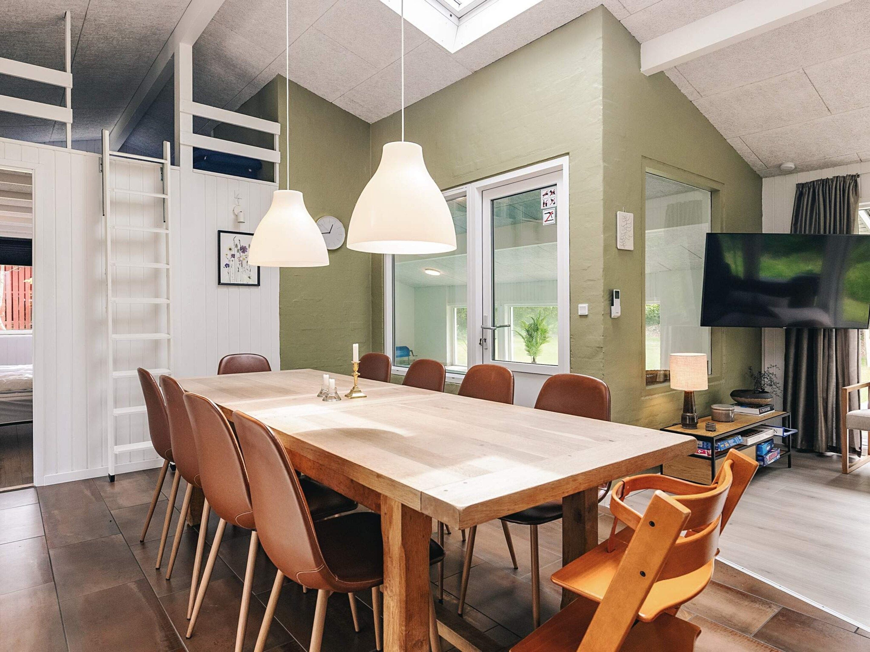 Un comedor con una mesa y sillas de madera, luces colgantes, un televisor y un ventanal con vistas.