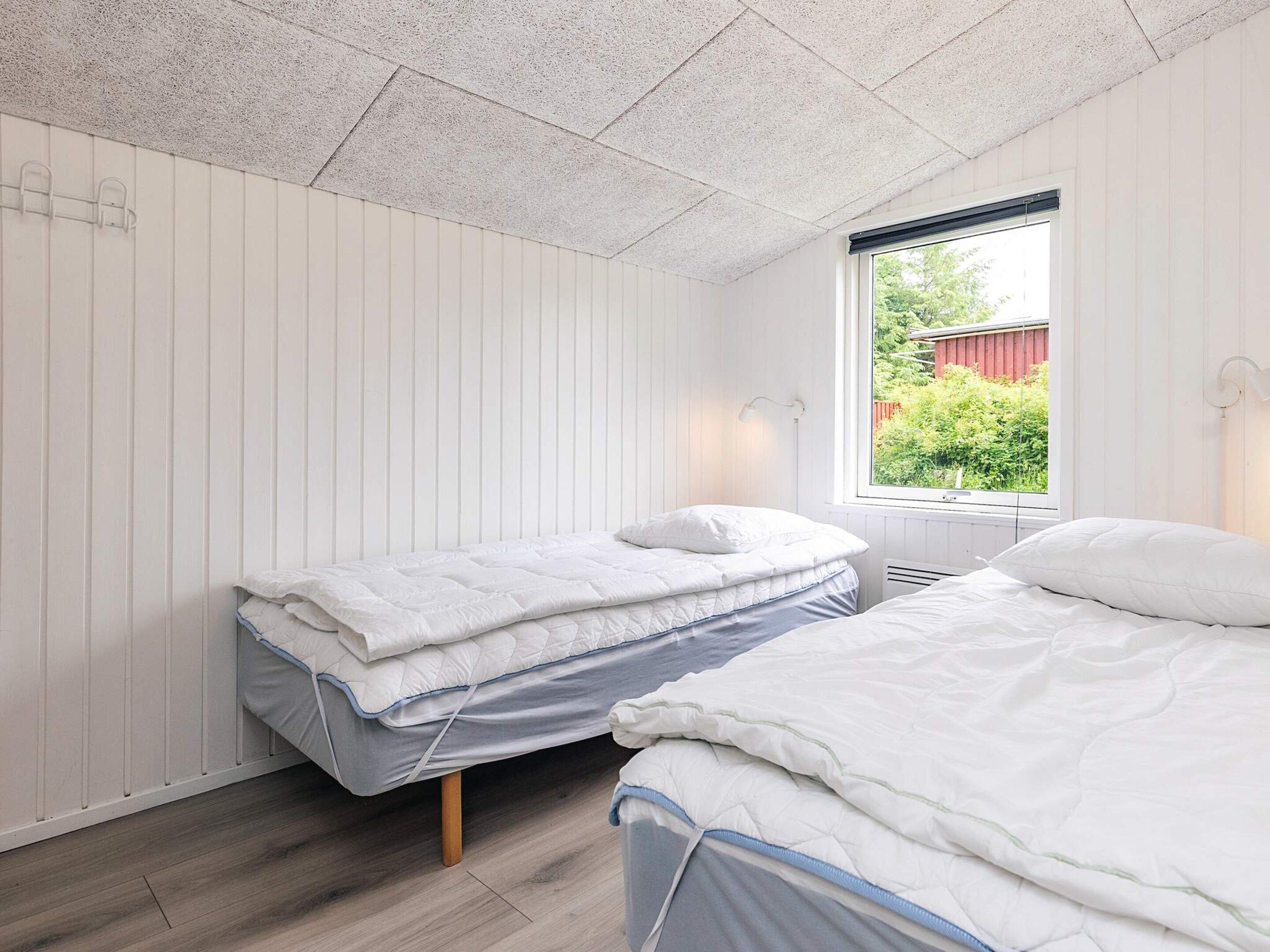 A bedroom with two beds, a window with a view of greenery, and a sloped ceiling.