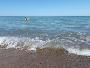 Una playa con olas, una persona en el agua y un cielo despejado.