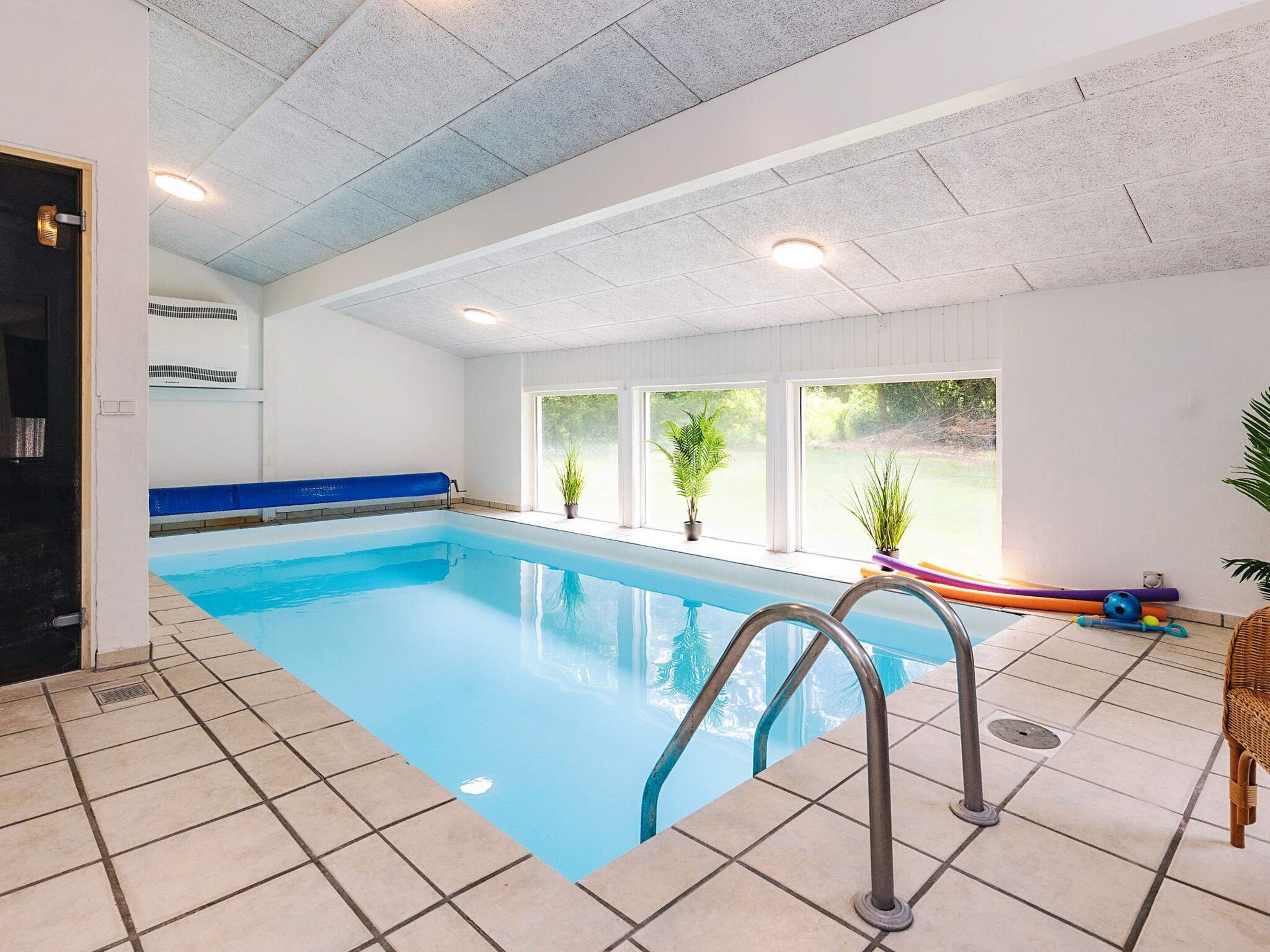 An indoor swimming pool with tiled flooring, a blue pool edge, and metal handrails.