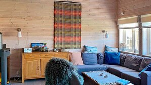 A cozy living room with a wooden cabin interior, featuring a sofa, a coffee table, a cabinet, and a large window providing natural light. - 10 Person Holiday Home in Rauland (Vinje)