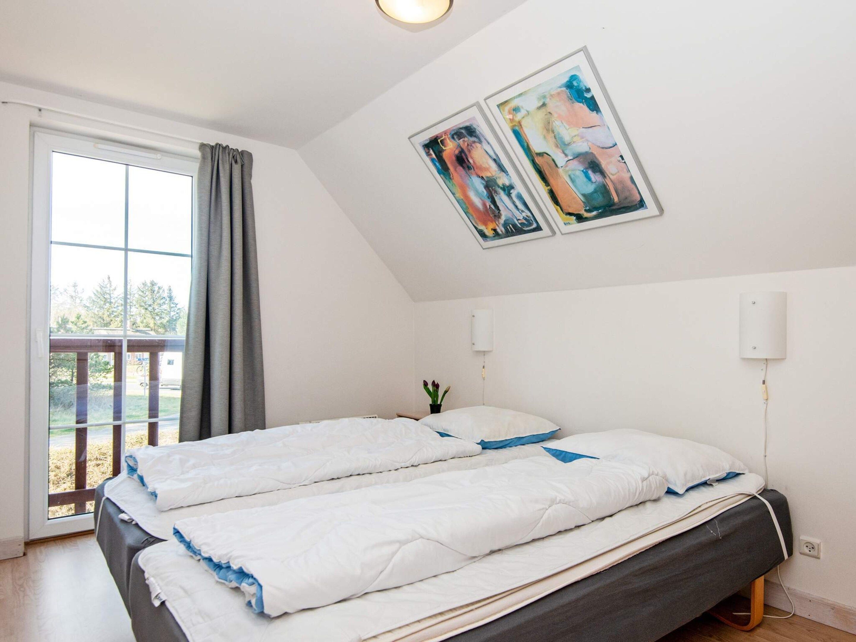 A bedroom with a bed, a window with curtains, and two wall-mounted light fixtures.