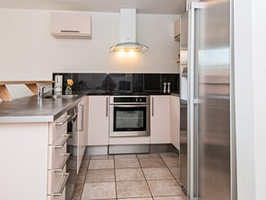 Una cocina moderna con horno integrado, refrigerador de acero inoxidable y protector contra salpicaduras negro en la encimera.