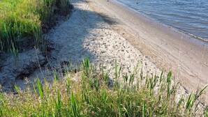 Ein Strand mit Sand und Gras, ein klarer Himmel und ruhiges Meer.