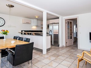 Una cocina moderna con refrigerador empotrado, una zona de comedor con mesa y sillas de madera, y un reloj en la pared.