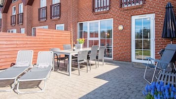 Een bakstenen gebouw met een terras, compleet met een tafel, stoelen en lounge fauteuils.