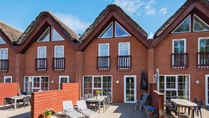 Eine Reihe Ziegelfassadenhäuser mit Strohdächern, Außenbestuhlung und einer gepflasterten Terrasse.
