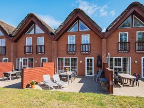 A row of brick houses with thatched roofs, outdoor seating, and a paved patio area. - 8 Person Holiday Home in Romo (Rømø)