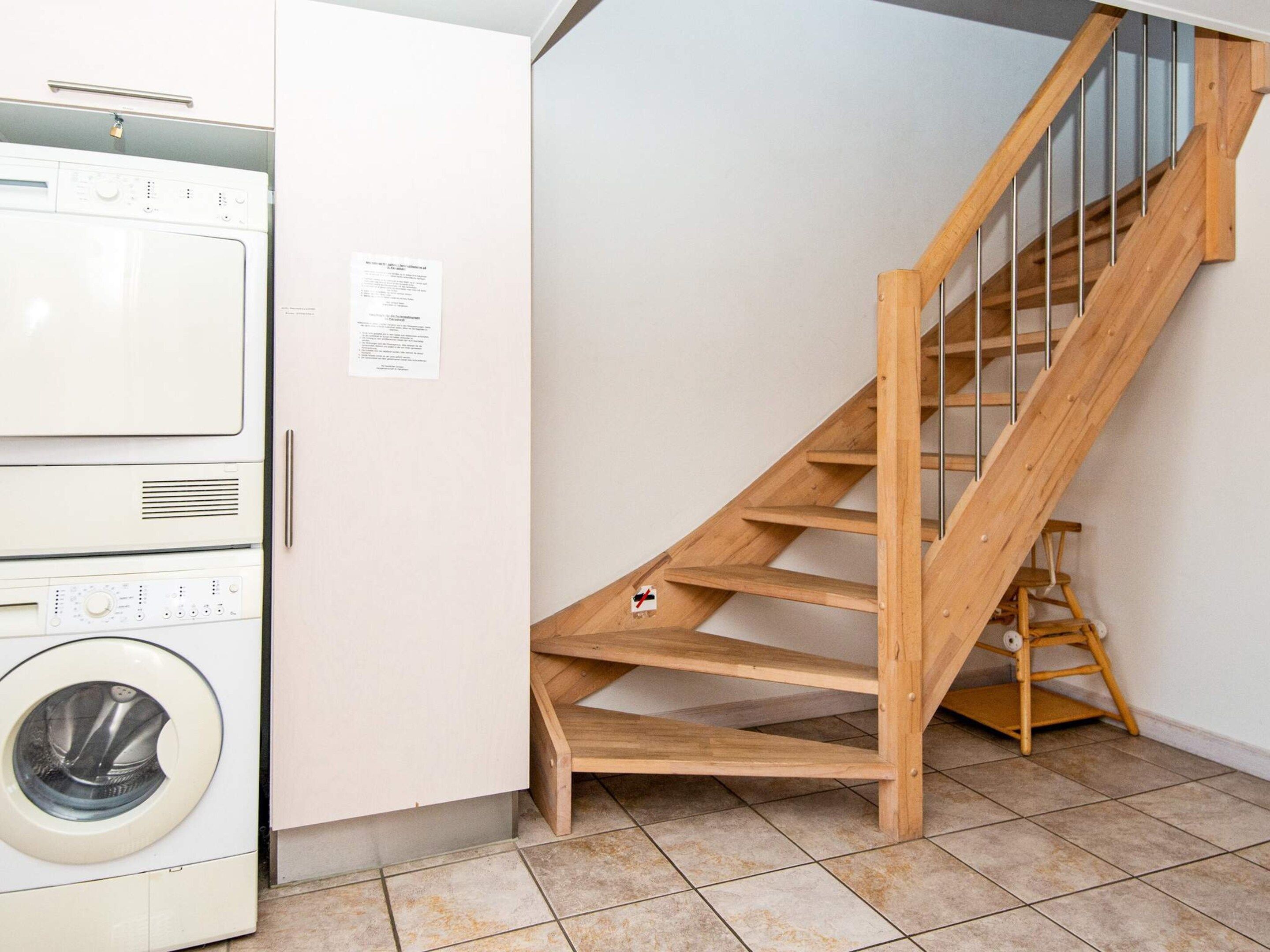 A laundry room with stacked washing machines and a wooden staircase.