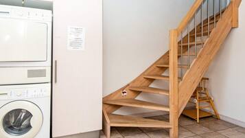 A laundry room with stacked washing machines and a wooden staircase.