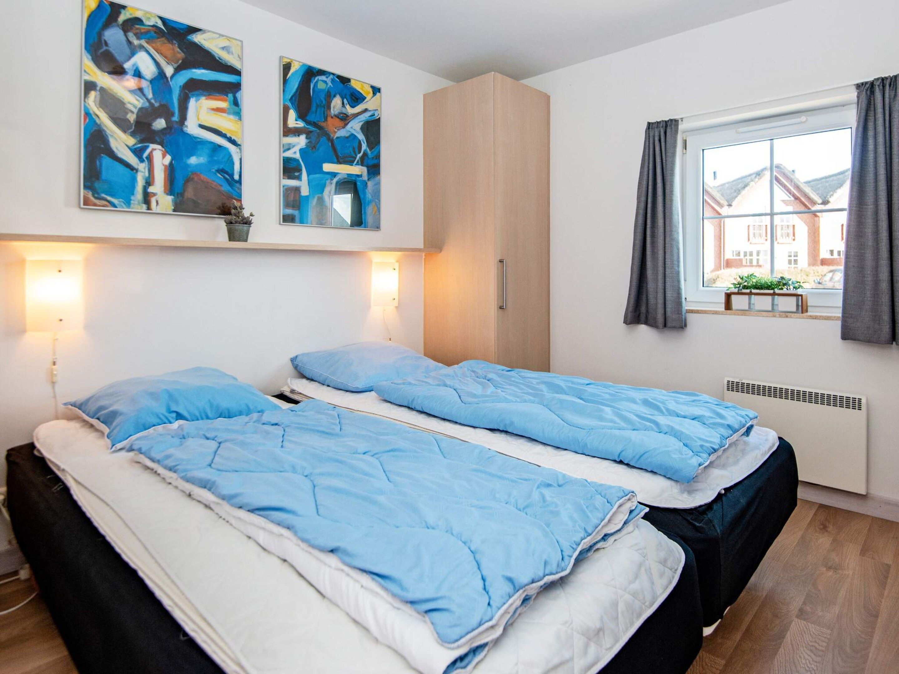 A bedroom with two beds, a wardrobe, abstract art on the wall, a window with curtains, and a radiator.