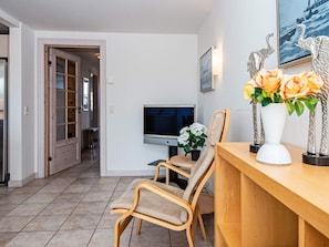 A modern living room with a television, a dining area with chairs, a wooden table, and decorative vases with flowers.
