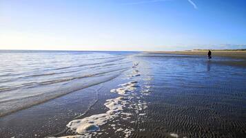 A beach with waves, a person walking, and a clear sky.