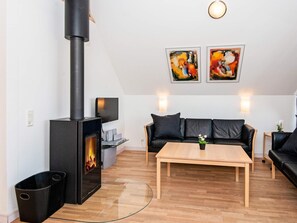 A modern living room with a wood-burning stove, a sofa set, a coffee table, and two paintings on the wall. - 8 Person Holiday Home in Romo (Rømø)