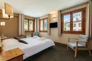 Une chambre d’hôtel avec un lit, un bureau, une chaise, une télévision et de grandes fenêtres avec des rideaux.