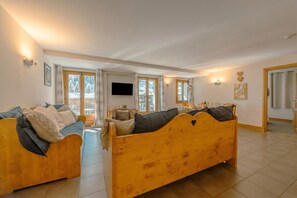 A spacious living area with a large wooden sofa, a television mounted on the wall, and a view of a snowy landscape through the windows.