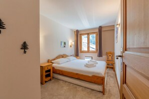 Un dormitorio con cama de madera, una mesita de noche, una pequeña silla de madera, una ventana con cortinas y una puerta.