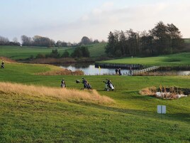 A golf course with a pond, a wooden bridge, and a few people playing.