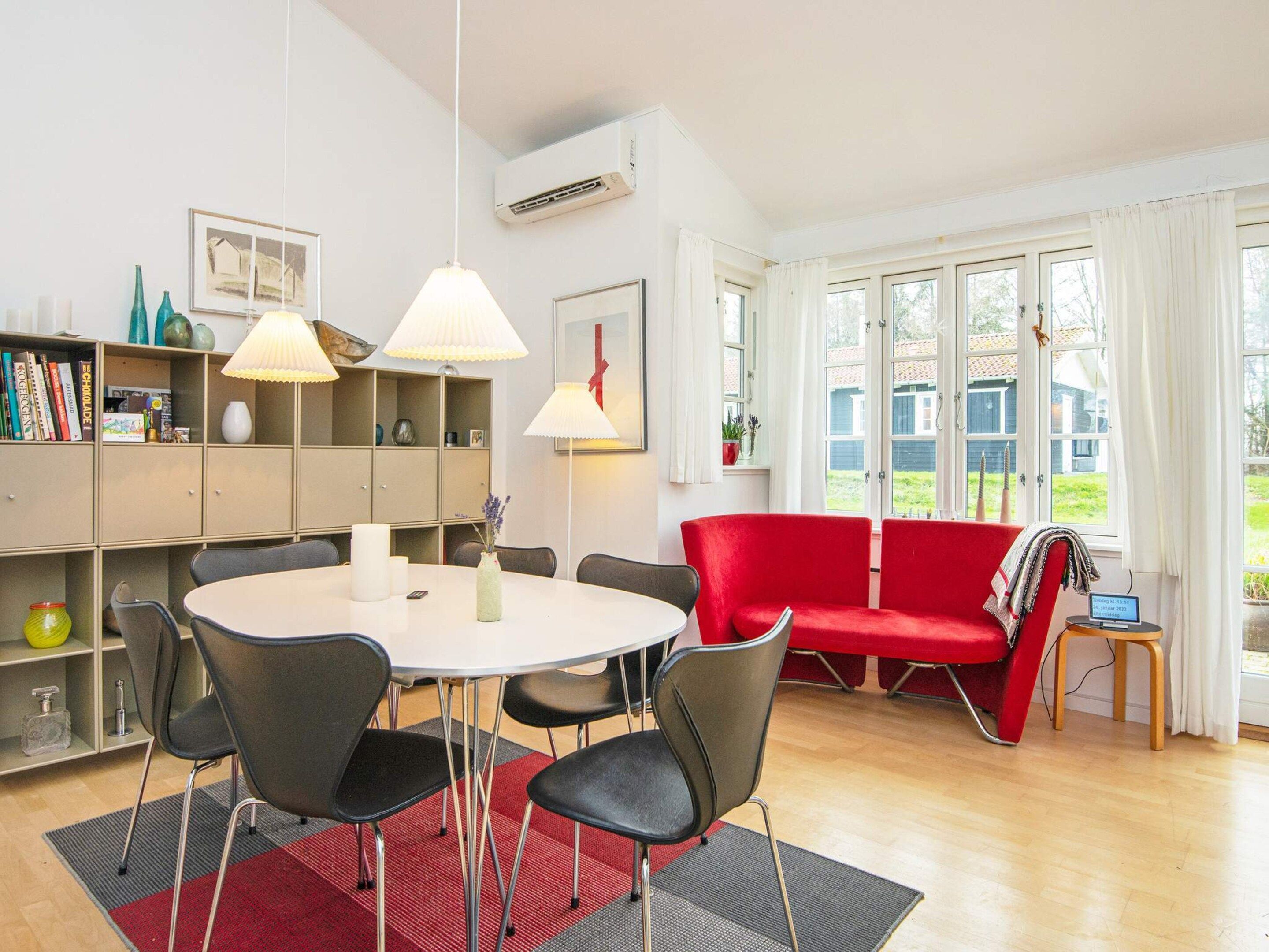 A modern living room with a round dining table, black chairs, a red sofa, and a bookshelf.