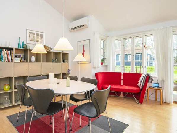 Un salon moderne avec une table à manger ronde, des chaises noires, un canapé rouge et une bibliothèque.
