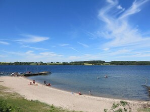 Une plage au bord d’un lac, avec une jetée, un ciel dégagé et une eau calme.