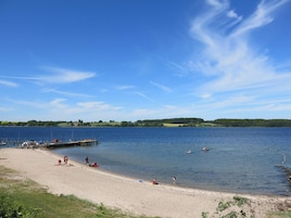 A lakeside beach with a pier, clear skies, and calm water.