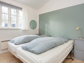 Une chambre avec deux lits, une table de chevet avec une lampe, un miroir rond et une fenêtre avec des rideaux.