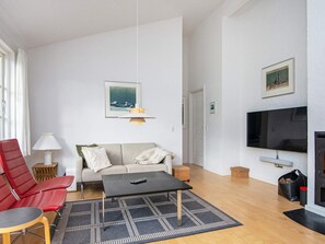 Una sala de estar moderna con un sofá, sillas rojas, una mesa de centro, un televisor y una chimenea.
