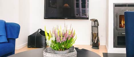 A living room with a black sofa, a television mounted on the wall, a fireplace, and a remote control on a table.