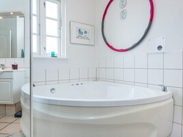 A bathroom with a large bathtub, a window, a mirror, and a toilet.