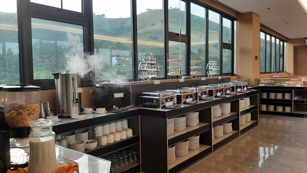 A buffet setup with steam rising from the food, a coffee station, and a view of hills through large windows. - Venus Royale Hotel (Coron)
