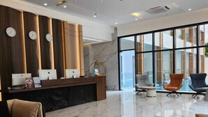 A modern lobby with marble flooring, a reception desk, seating area, and large windows offering a view of the outdoors. - Venus Royale Hotel (Coron)