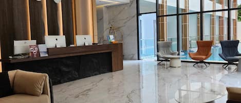 Un vestíbulo moderno con suelo de mármol, mostrador de recepción, zona de estar y amplias ventanas con vistas al exterior.