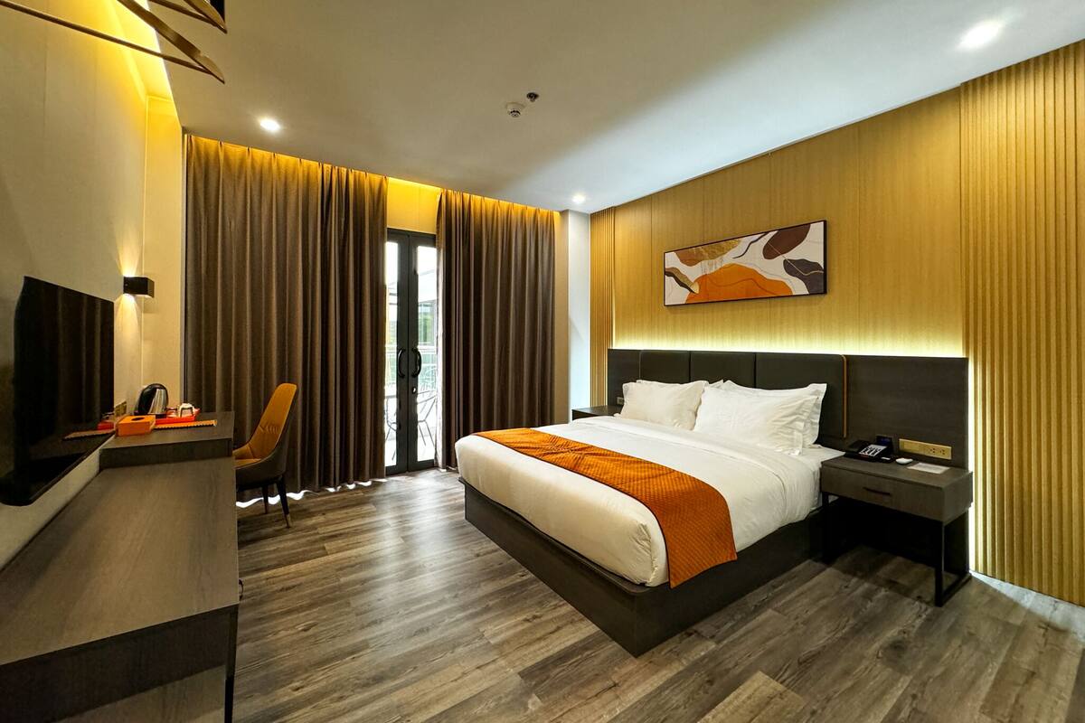 A modern hotel room with a large bed, a desk with a chair, a nightstand, and a painting on the wall.