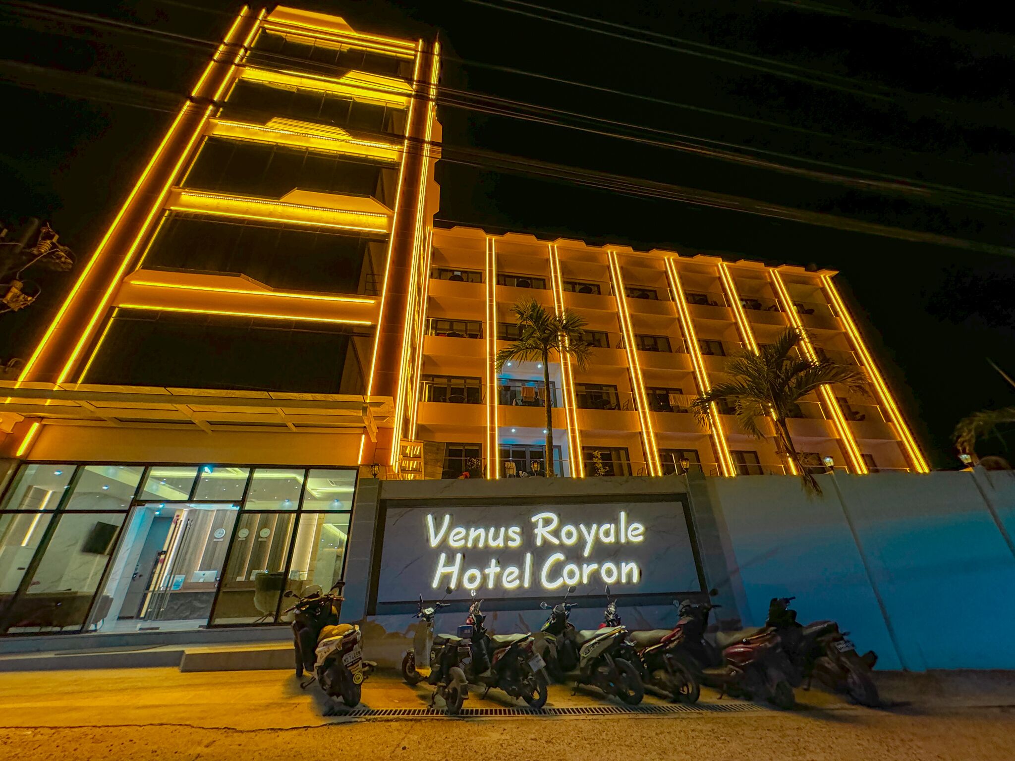 Exterior del Hotel Venus Royale Coron de noche, con líneas verticales iluminadas y un cartel.