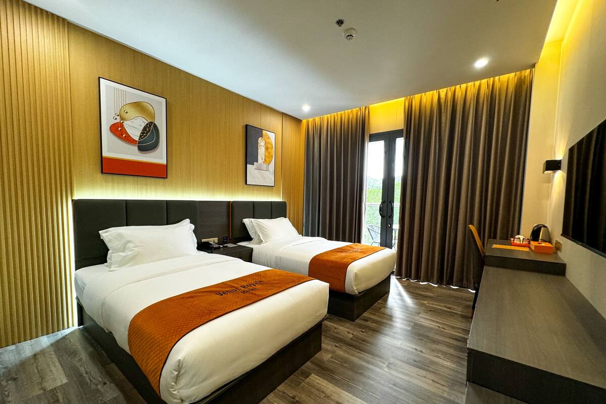 A hotel room with two beds, wooden flooring, and a balcony with curtains.