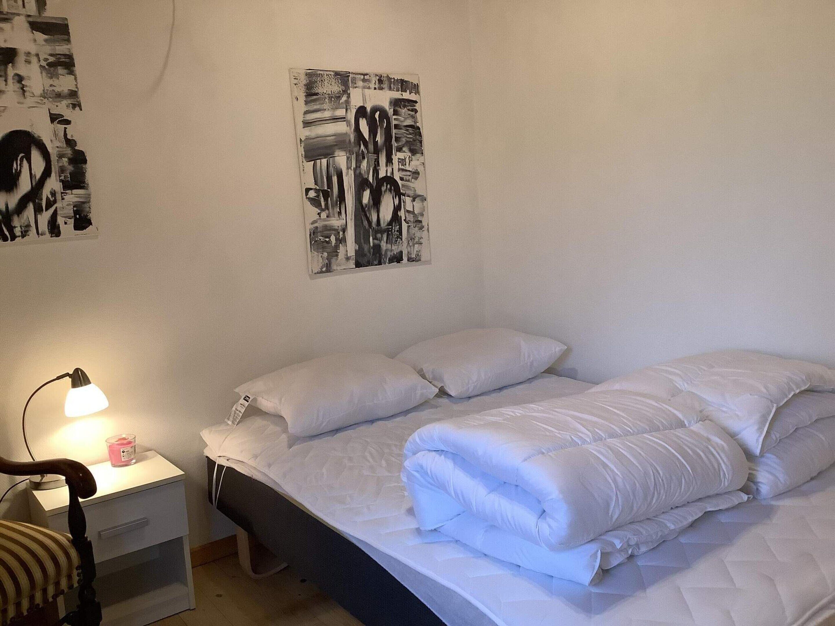 A bedroom with a bed, white pillows, a bedside table with a lamp, and a chair.
