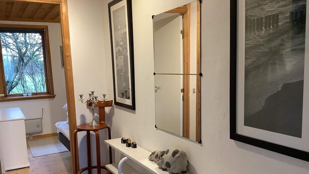 A small, well-lit room with a wooden ceiling, a window with a view of trees, a white desk, a mirror, and a shelf with decorative items. - 6 Person Holiday Home in Bedsted Thy (Bedsted)