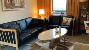 A cozy living room with a black leather sofa, a white coffee table, a wooden chair, a fur rug, and a painting on the wall. - 6 Person Holiday Home in Bedsted Thy (Bedsted)