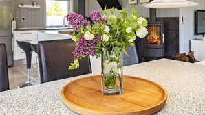 A modern kitchen with a central island, a fireplace, and a vase with flowers on a wooden tray. - 4 Person Holiday Home in Vinderup (Vinderup)