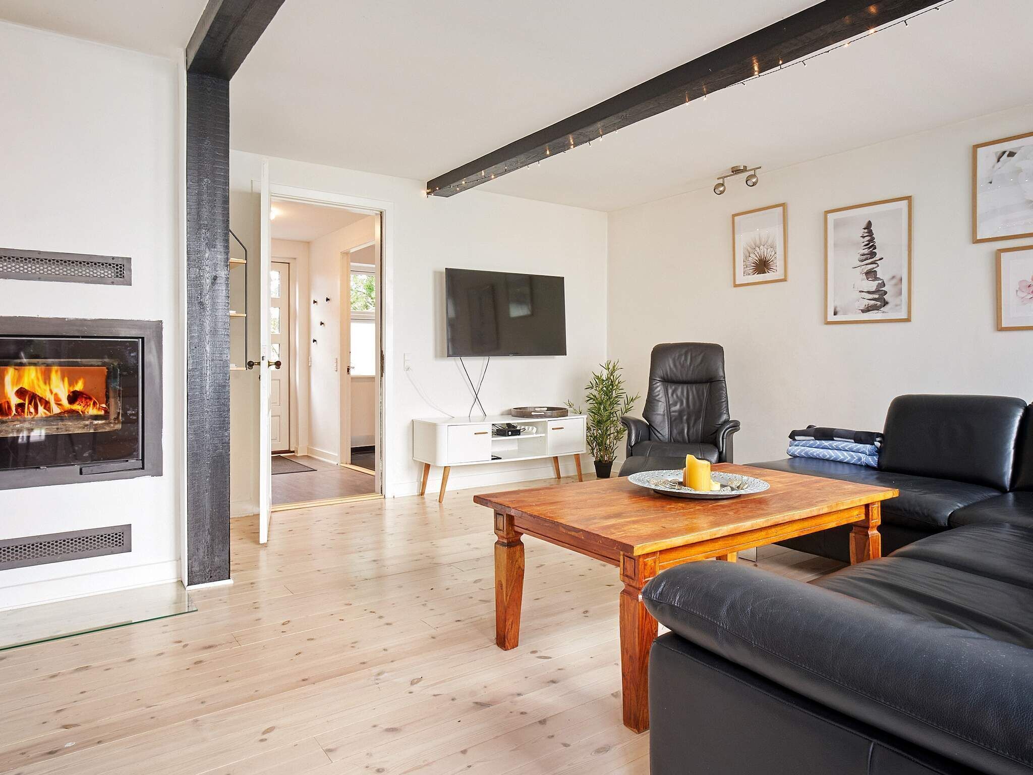 Un salon moderne avec une cheminée, un canapé en cuir noir, une table basse en bois et un téléviseur à écran plat fixé au mur.