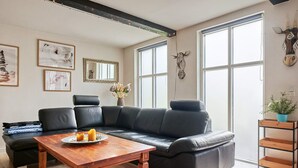 Ein modernes Wohnzimmer mit einem schwarzen Leder-Modulsofa, einem Holztisch und einem großen Fenster, das natürliches Licht hereinlässt.