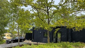 Eine moderne schwarze Hütte mit einer kleinen Veranda und einem geparkten Auto in der Nähe.