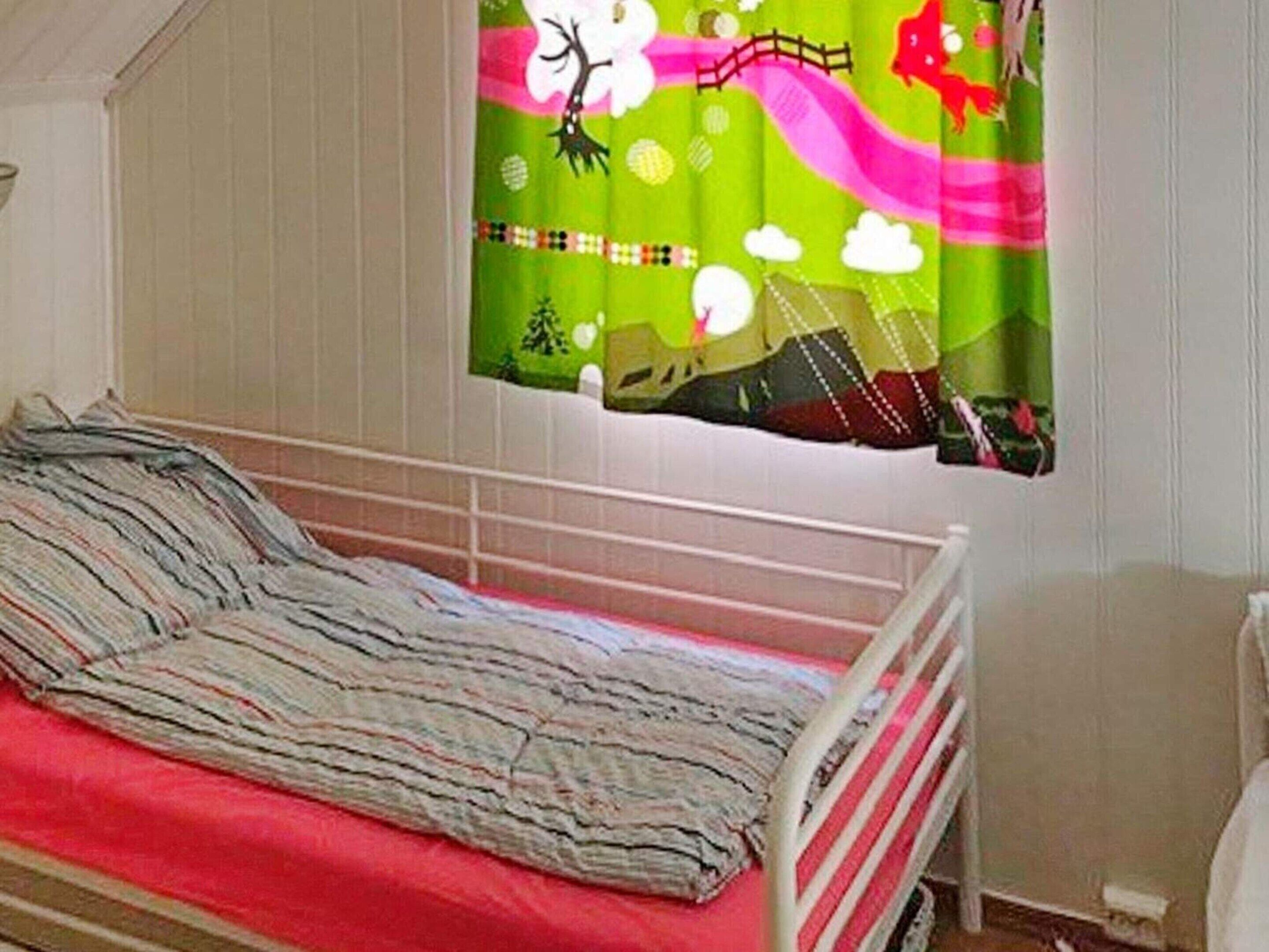 A single bed with a striped blanket, a white headboard, and a colorful curtain depicting a landscape scene.