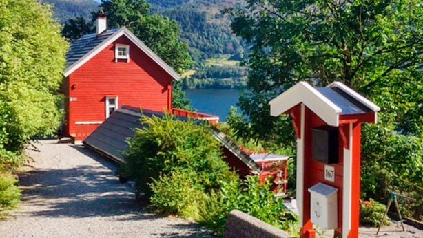 A red cabin with a gravel path leading to it, surrounded by greenery and a lake. - 4 Star Holiday Home in Bruvik (Masfjorden)