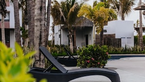 Un espace aménagé au bord de la piscine, avec des chaises longues, des palmiers et un petit arbuste aux fleurs roses.