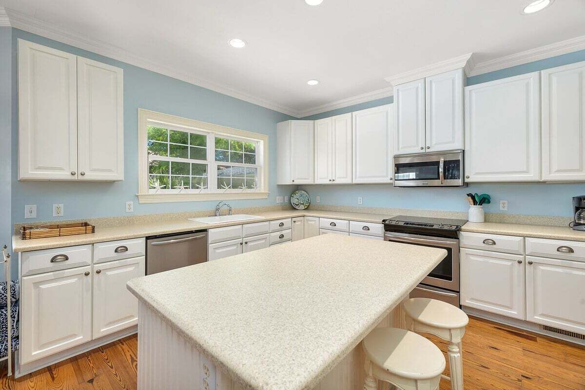 A kitchen with white cabinets, a central island, a microwave, and a sink.